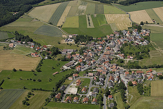 Dorf umgeben von Feldern und Wiesen mit vereinzelten Bäumen