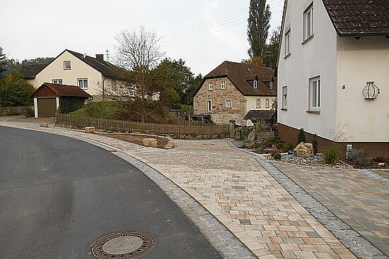 Straße mit Gehweg vorbei an Häusern mit Grünflächen